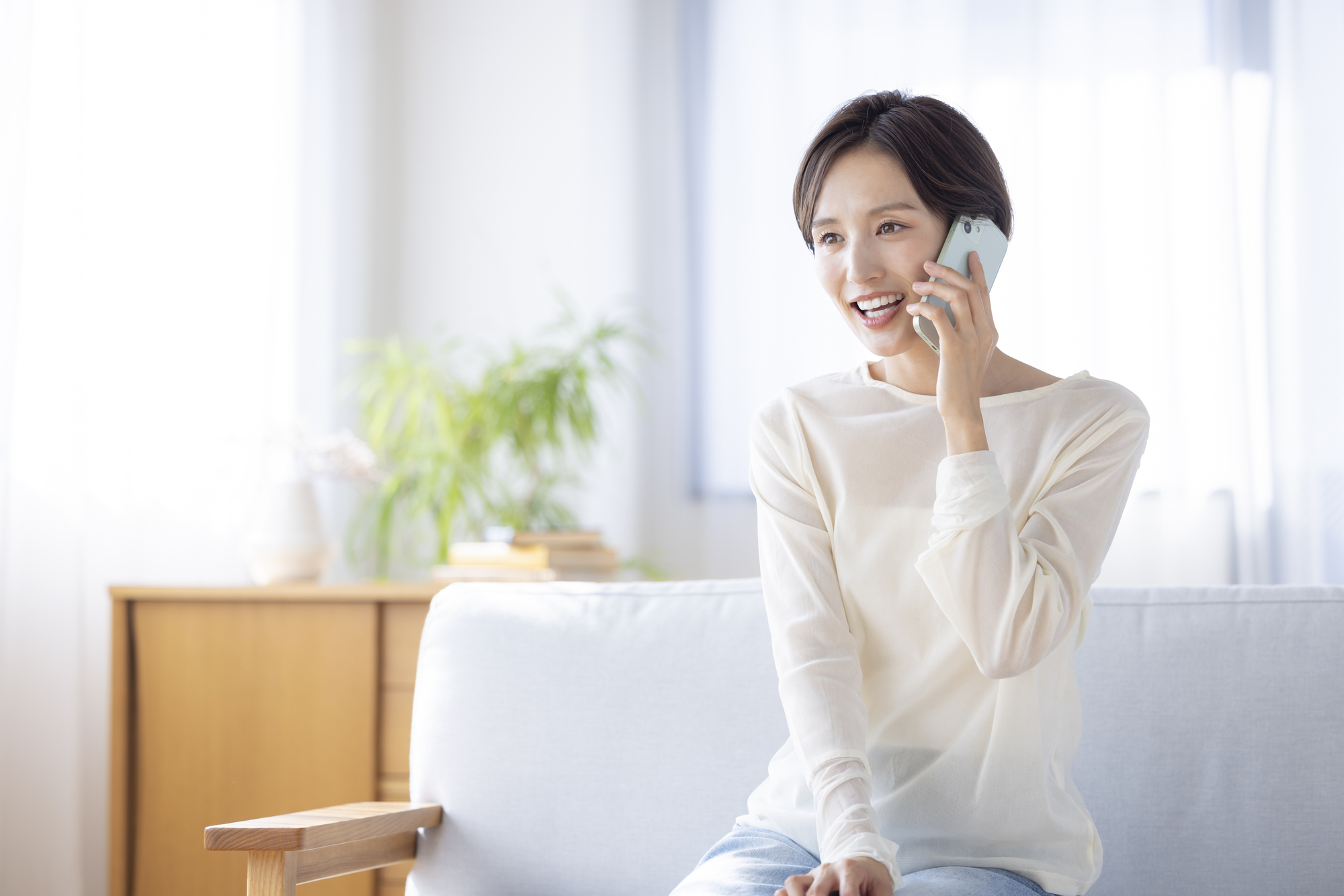 自宅でスマートフォンを使って電話する女性のイメージ